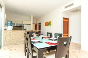 A dining area with a table set for four, a kitchen in the background, and a door with a colorful painting.