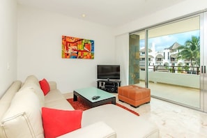 A modern living room with a sofa, a coffee table, a TV, and a colorful abstract painting. - Rooftop Pool and Ocean Views, Walk to Coco Beach (Playa del Carmen)