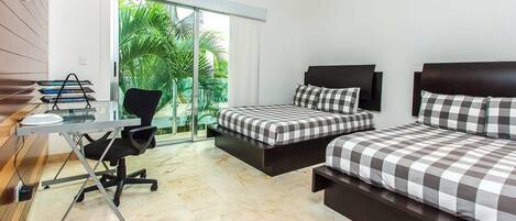 A hotel room with a desk, two beds, a chair, and a view of greenery.
