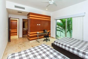 A hotel room with two beds, a desk, and a view of greenery through the window.