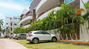 A modern building with a curved balcony, parked cars, and palm trees.