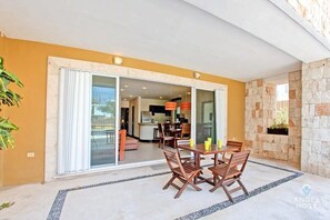A patio with a table and chairs, a sliding glass door leading to a kitchen, and a stone wall.