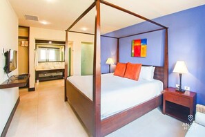 A four-poster bed with white bedding and orange pillows, a nightstand with a lamp, and a bathroom with a large mirror and dual sinks.
