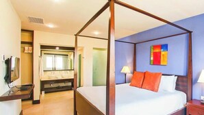 Un lit à baldaquin avec une literie blanche et des coussins orange, une table de chevet avec une lampe, et une salle de bain dotée d’un grand miroir et de deux vasques.