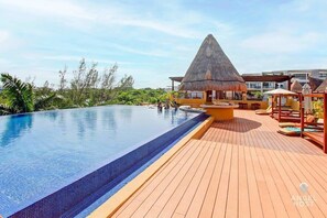 A swimming pool with a wooden deck and a thatched-roof structure.