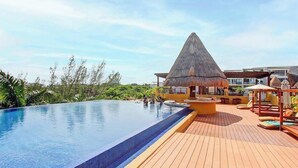 Une piscine dotée d’une terrasse en bois et d’une structure surmontée d’un toit de chaume.