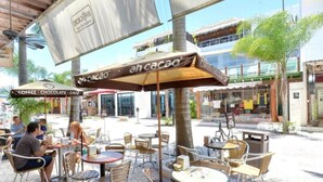 Un café en plein air avec des tables et des chaises, une enseigne indiquant « Ah Cacao », et un bâtiment en arrière-plan.