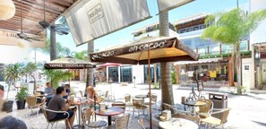 Un café al aire libre con mesas y sillas, un letrero que dice 'ah cacao' y un edificio al fondo.