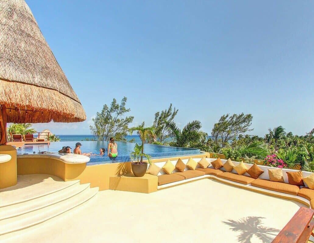 A resort pool area with a thatched roof, lounge chairs, and a view of the ocean.