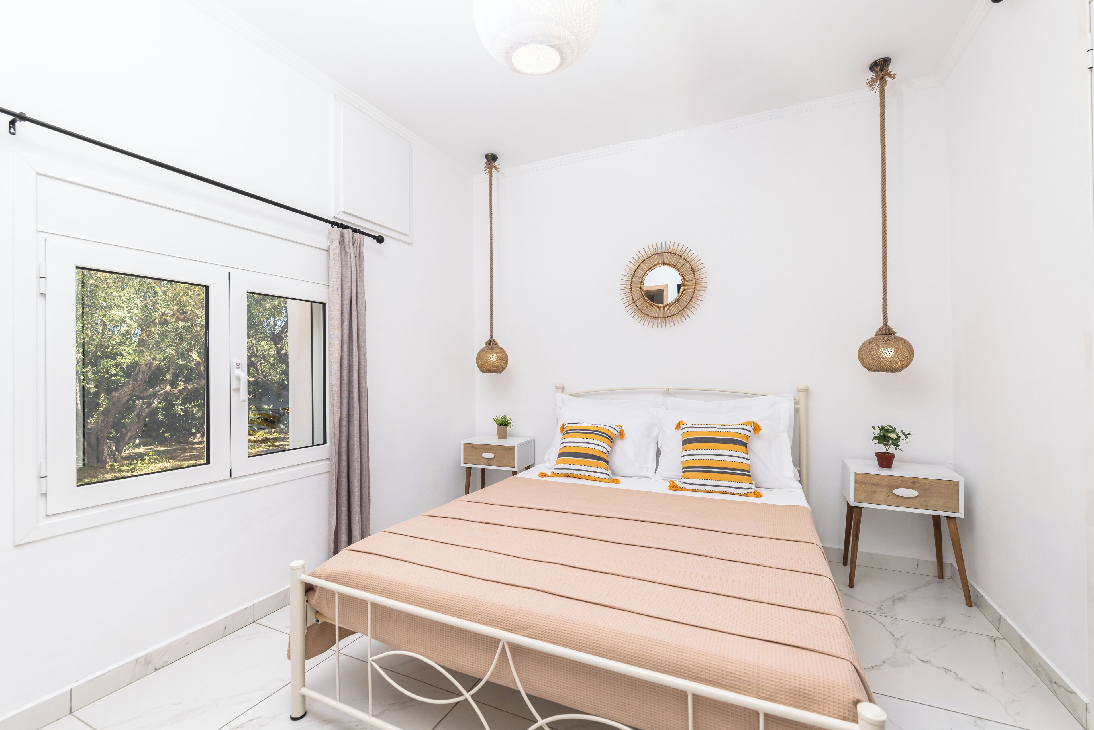A bedroom with a bed, two bedside tables, a window, and a wall-mounted mirror.