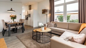 A modern living room with a sofa, coffee table, dining table, and kitchen in the background.