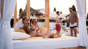 A wooden deck with a bed, a tray with items, and a pool area in the background.