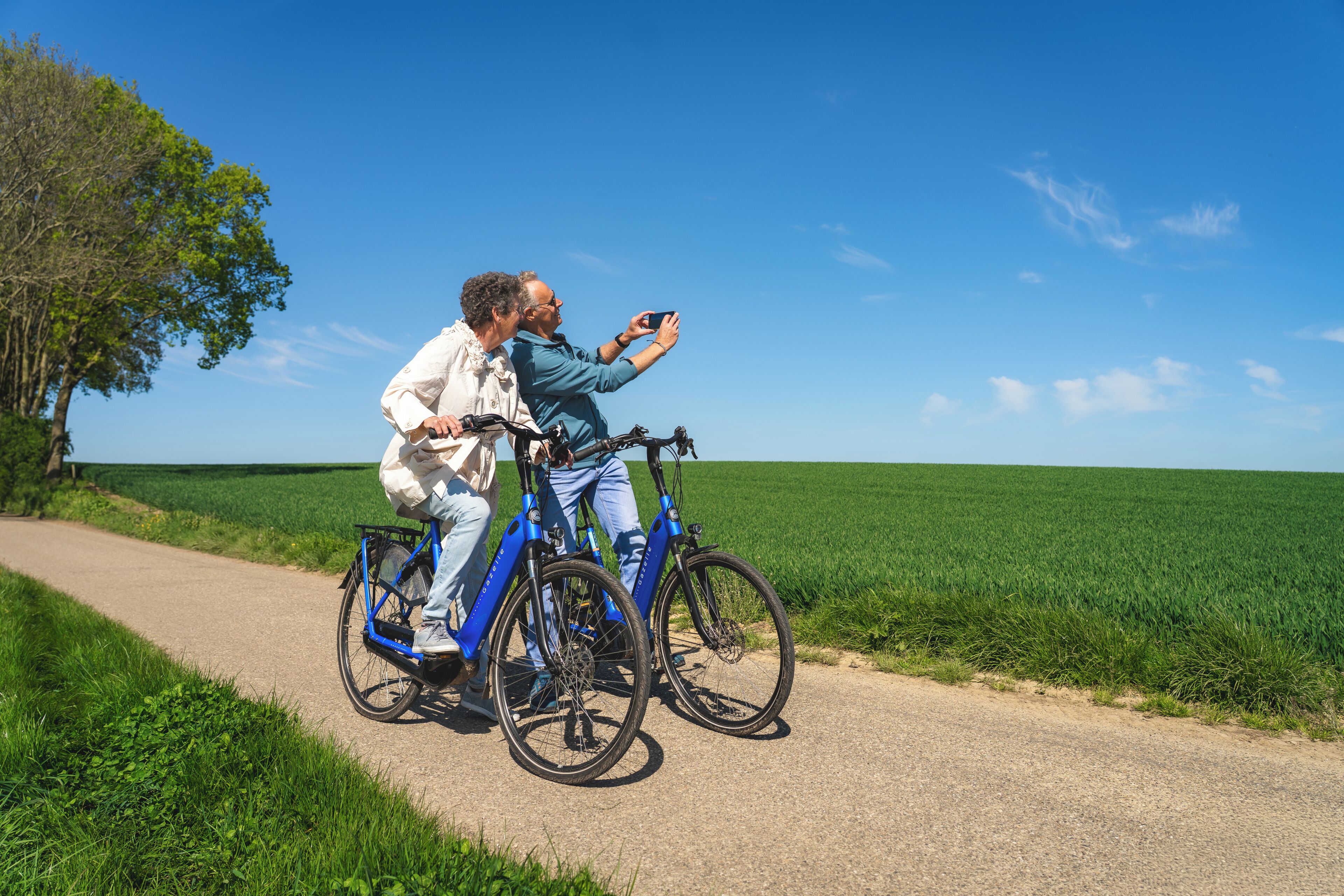 Deux personnes à vélo sur un chemin de campagne, avec un champ d’un côté et un ciel dégagé au-dessus d’elles.
