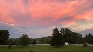 Un campo cubierto de hierba con una valla blanca, árboles y un cielo al atardecer.