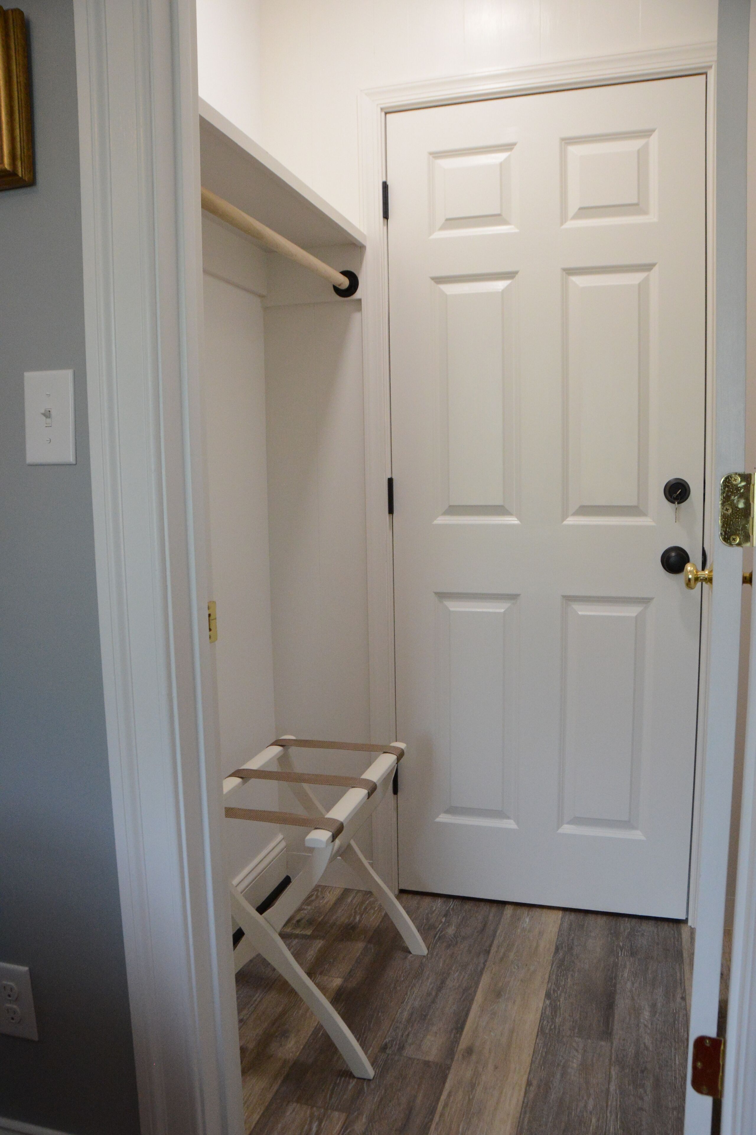 A room with a white door, a wooden floor, and a white bench against the wall.