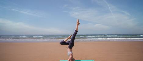 A person performing a handstand on a yoga mat on a beach with the ocean in the background.