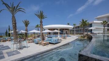 A resort pool area with lounge chairs, umbrellas, and a building with a curved roof.