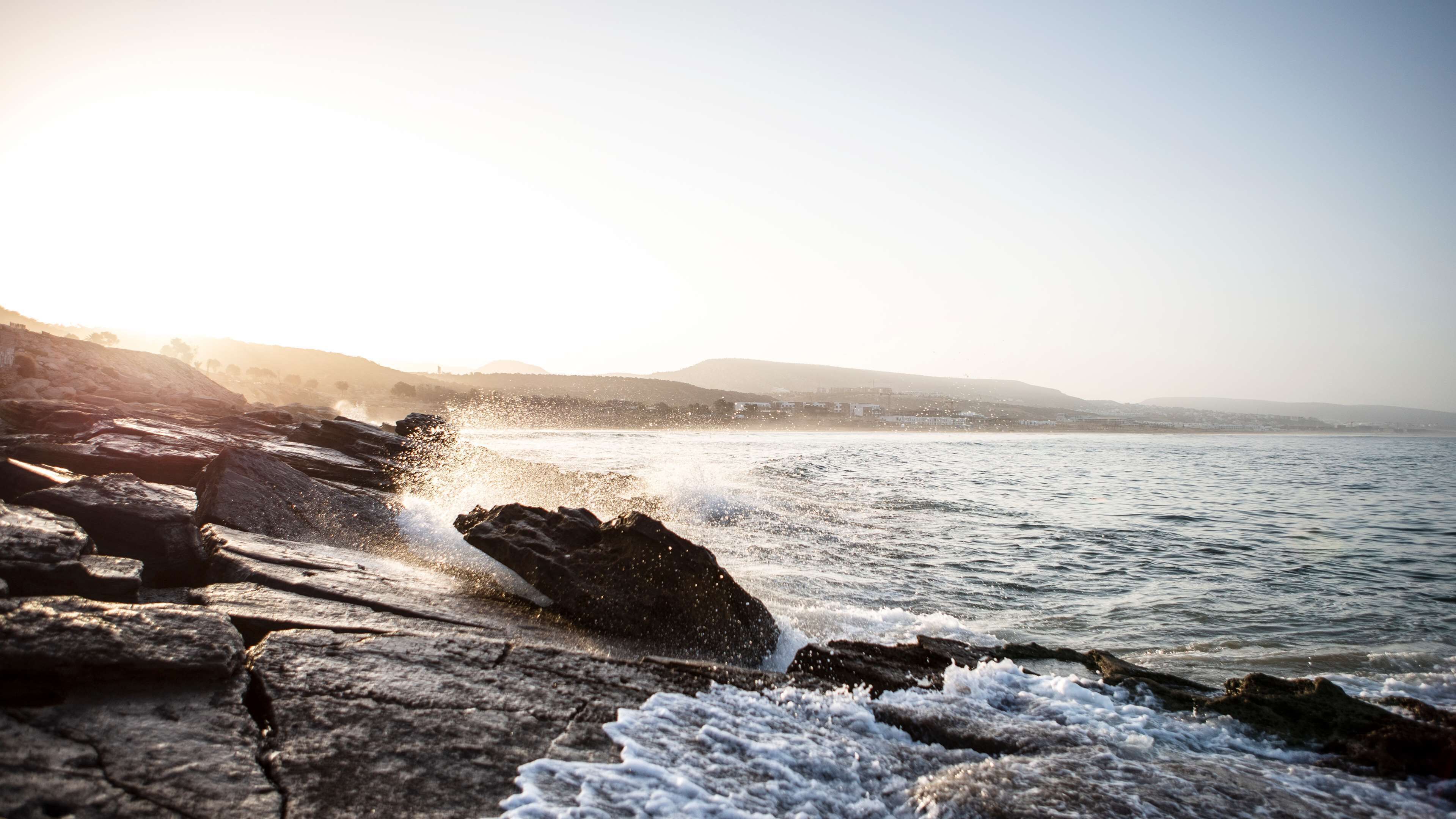 A rocky shoreline with waves crashing against the rocks under a clear sky.