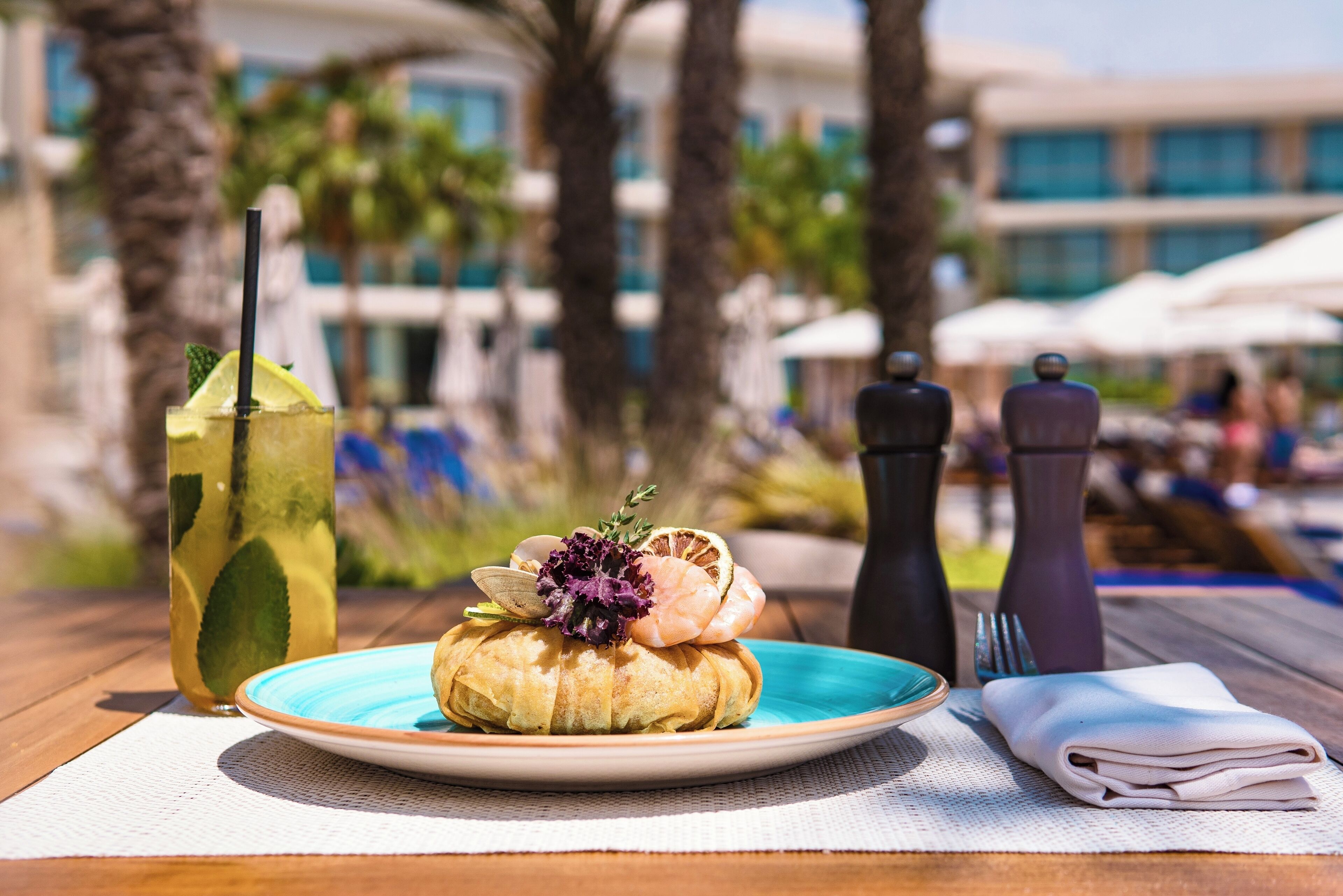 A table with a plate of food, a drink, and a folded napkin.