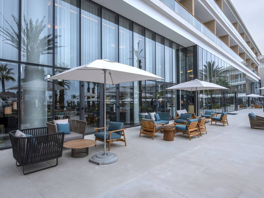 An outdoor seating area with modern furniture and umbrellas, in front of a building with large windows.