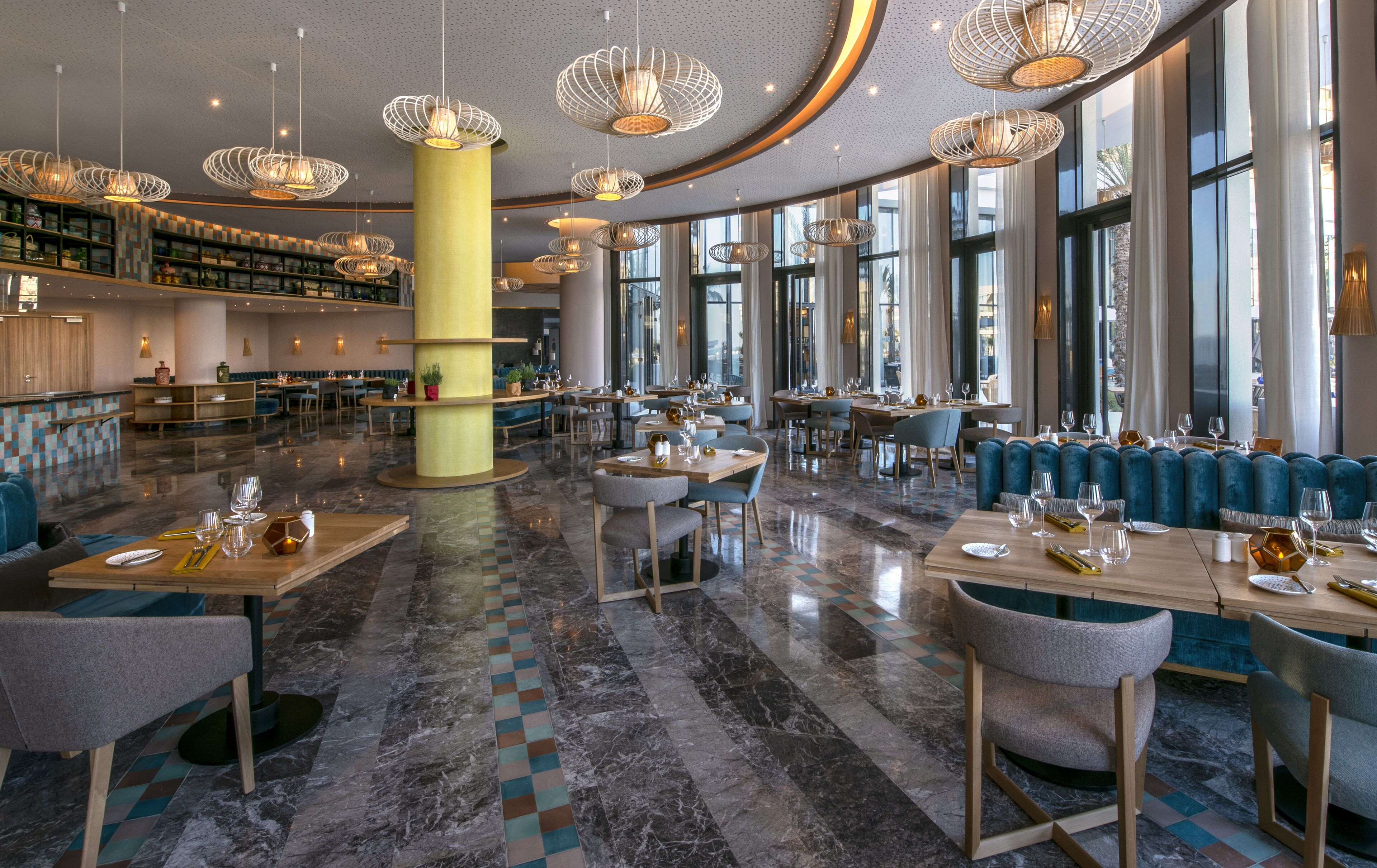 A spacious restaurant with high ceilings, modern chandeliers, and large windows.