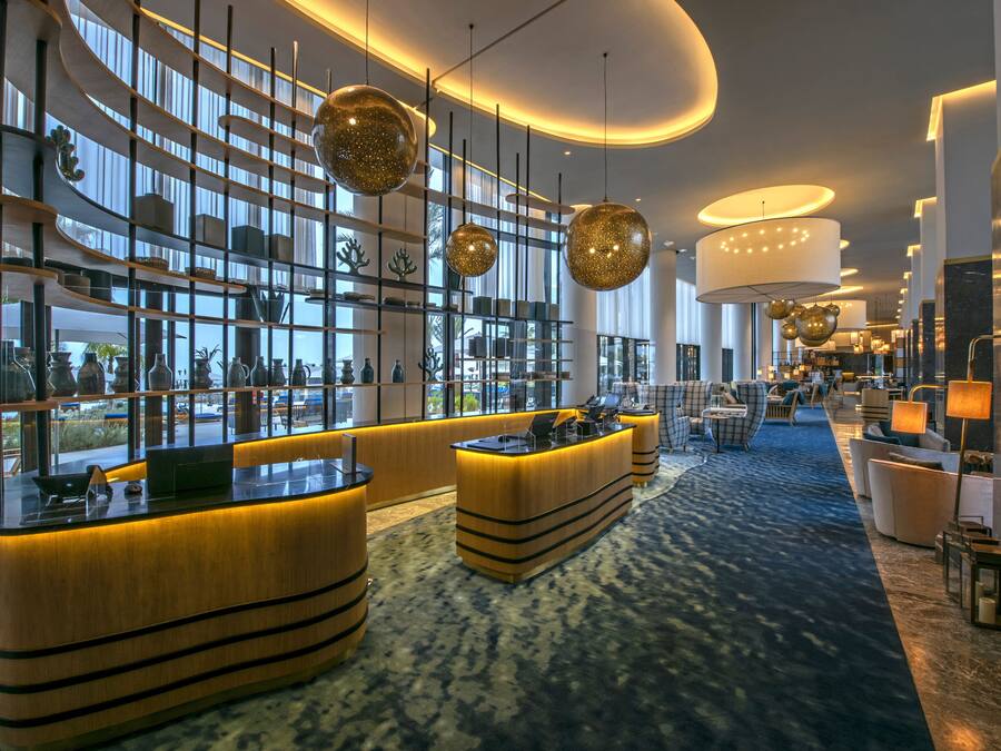 Un hall d’hôtel moderne doté d’un comptoir d’accueil, d’un espace salon et de grandes fenêtres offrant une vue sur la ville.