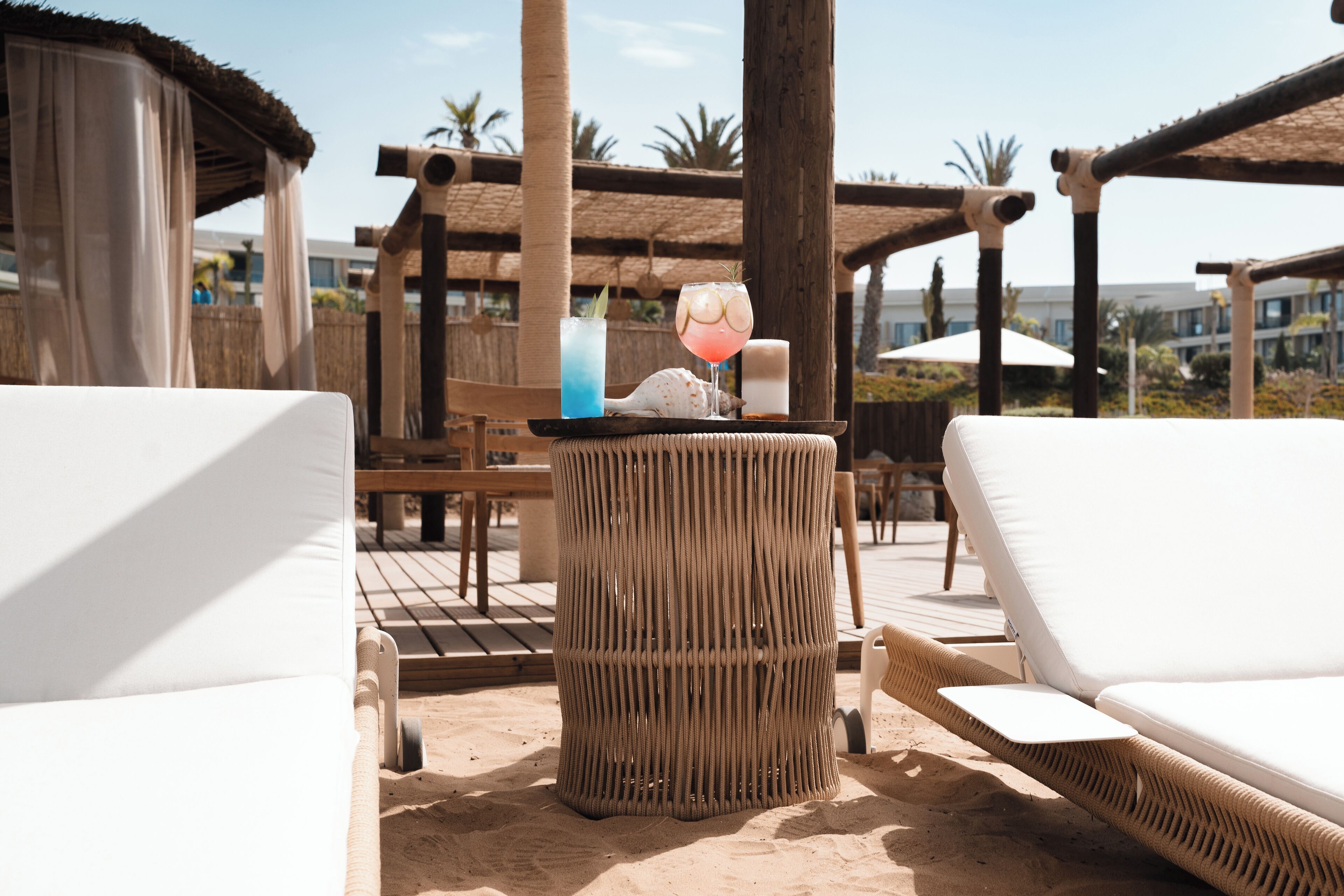 Ein Strandloungebereich mit Korbmöbeln, einem Getränketablett und einer dekorativen Meeresschnecke.