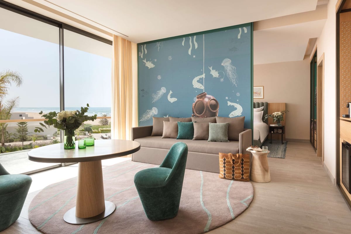A modern living room with a large window, a round table, and a sofa with decorative pillows.