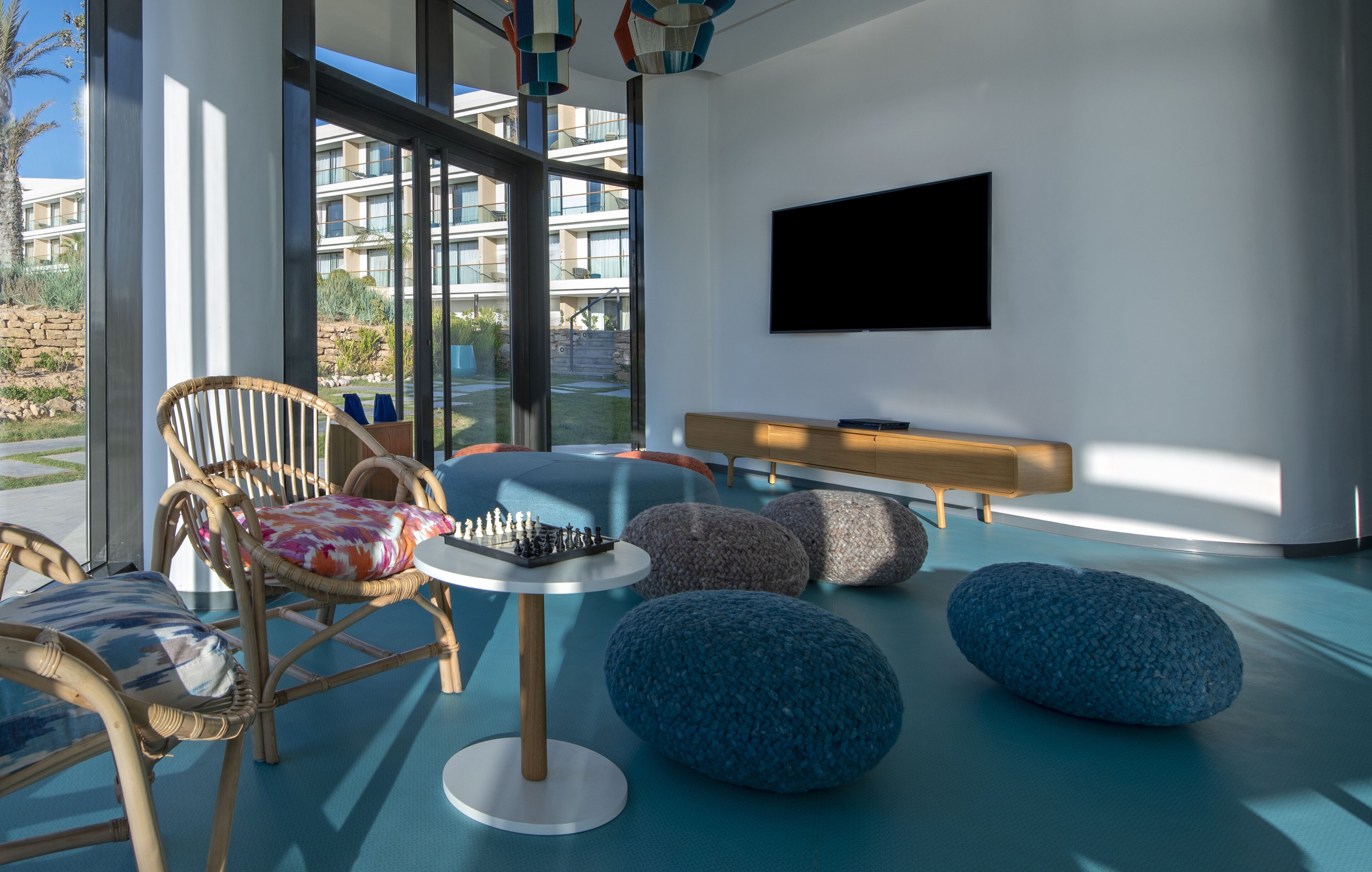 A modern lounge area with wicker chairs, a round table, and blue bean bags.