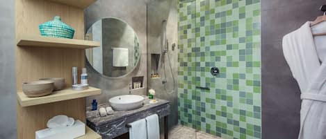 A modern bathroom with a marble sink, wooden shelves, a round mirror, and a shower with green mosaic tiles.