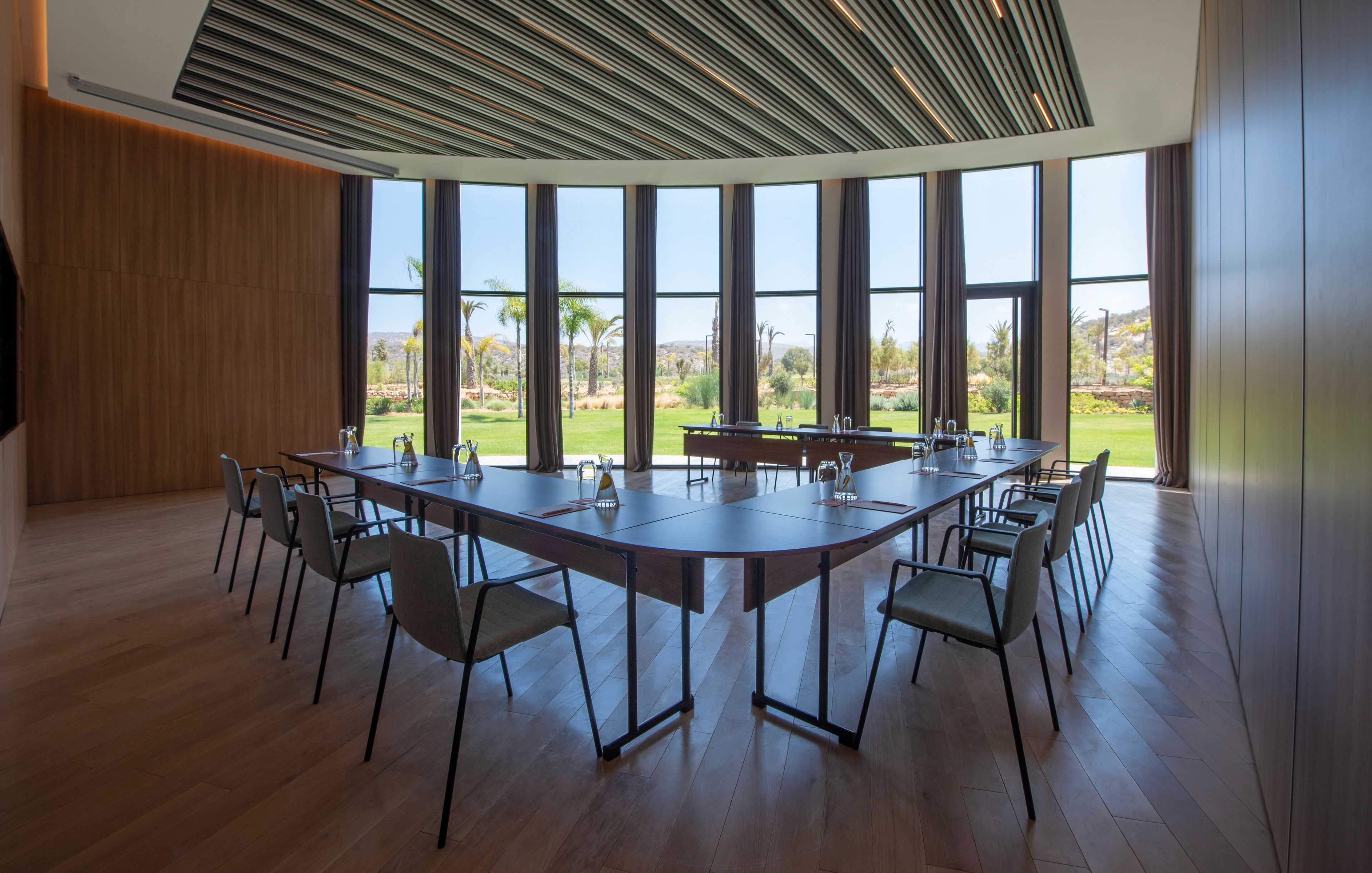 Ein Konferenzraum mit langem Tisch und Stühlen, große Fenster mit Blick auf eine angelegte Grünfläche.