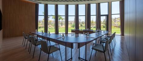 Un salón de conferencias con una larga mesa y sillas, amplias ventanas que dan a un jardín paisajístico.