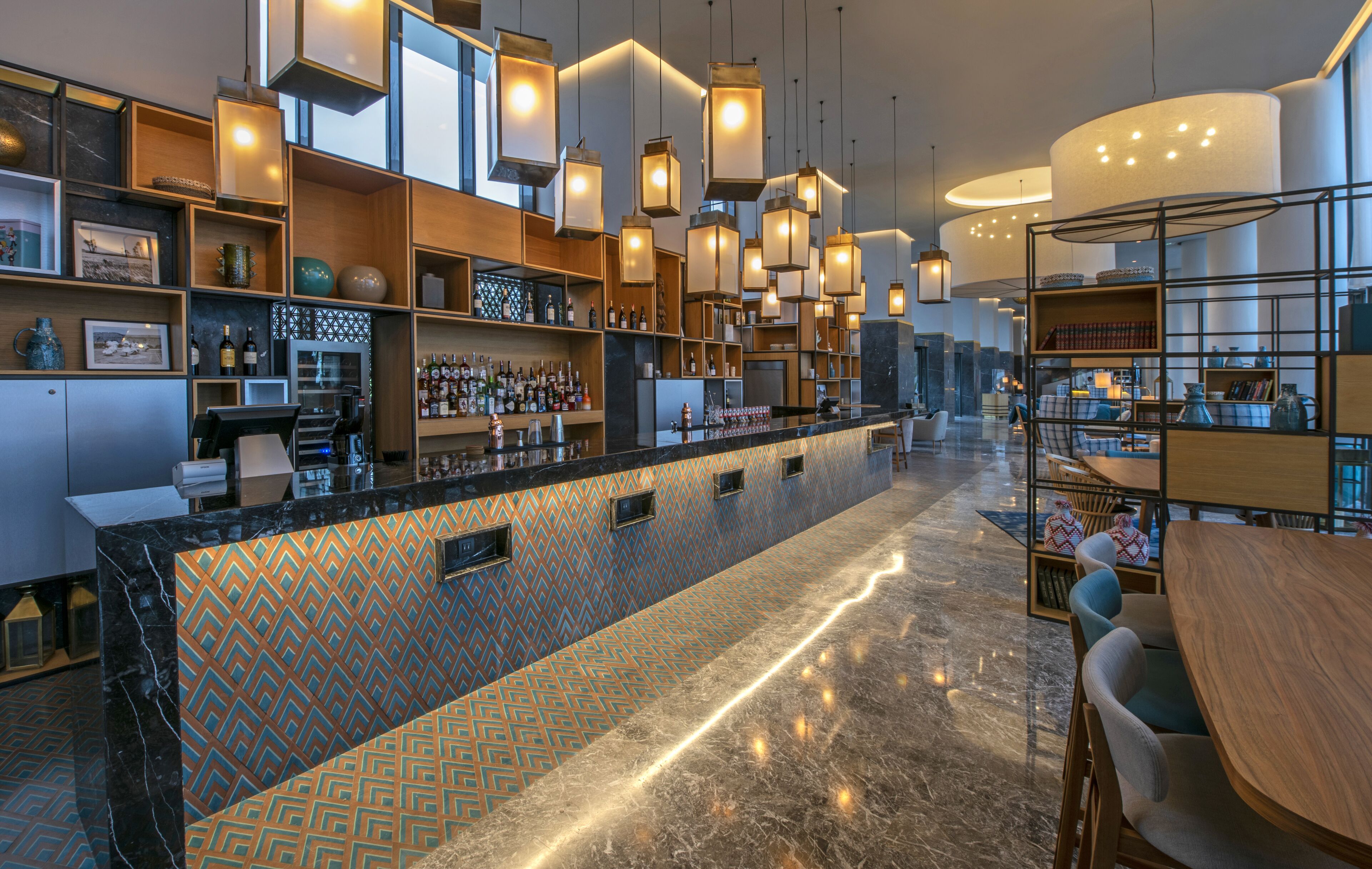 Un espace bar moderne avec un mur recouvert de carreaux décoratifs, des étagères remplies de bouteilles et des luminaires suspendus.