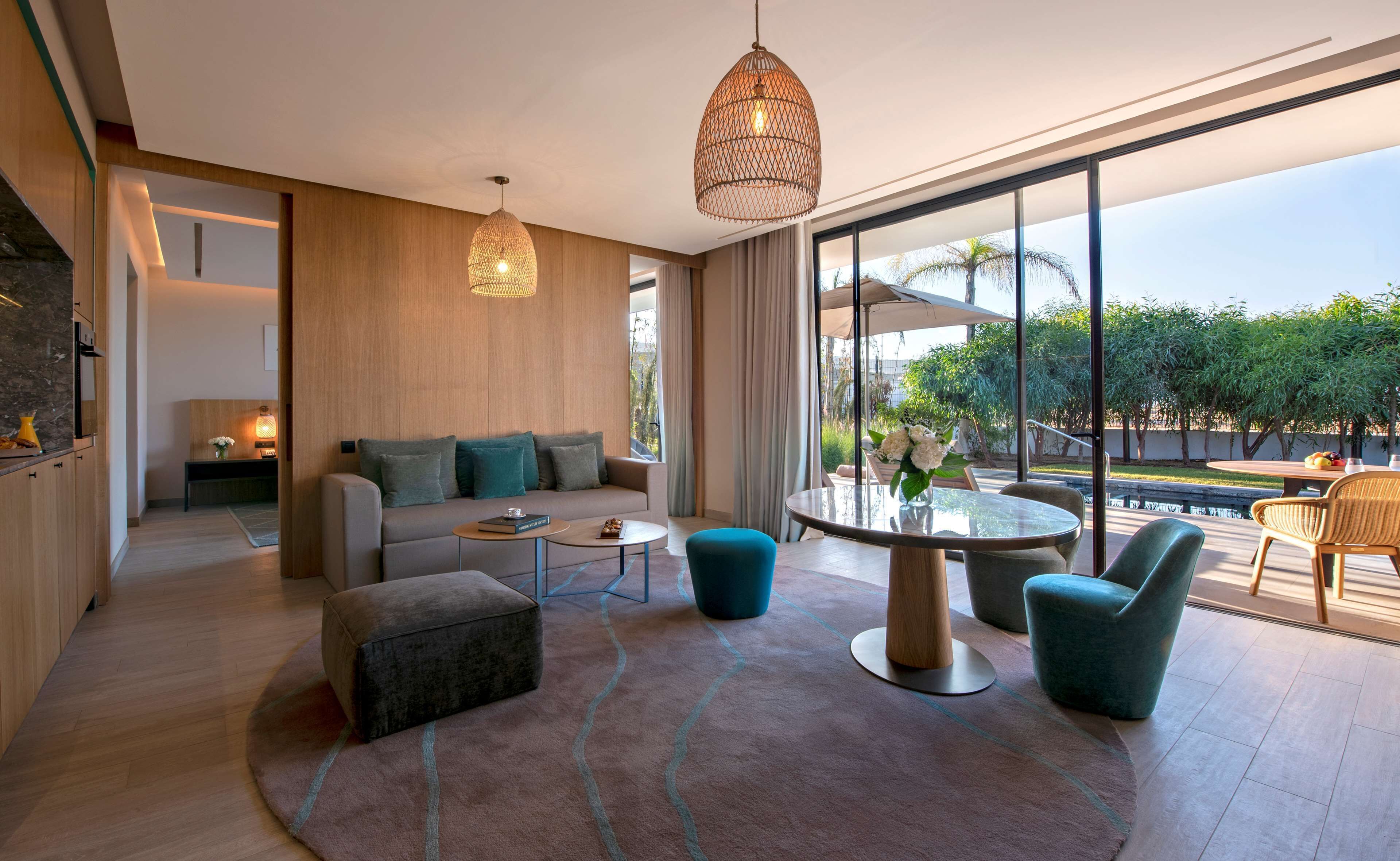 Una sala moderna con sofá, reposapiés, mesa de centro y sillones. Hay un ventanal con vistas a zonas verdes.