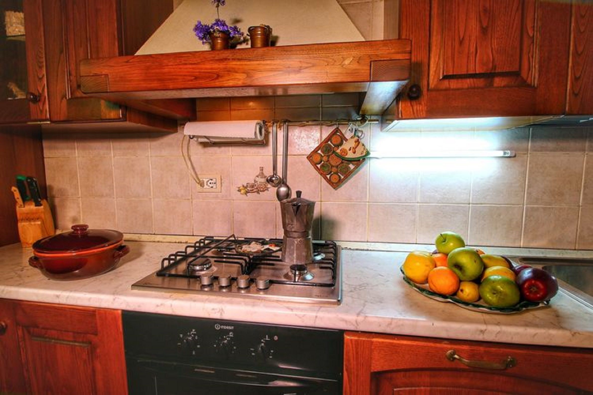 A kitchen with a stove, a dish rack, and a fruit bowl.