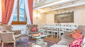 A spacious living room with antique furniture, a glass coffee table, and a dining area with white chairs.