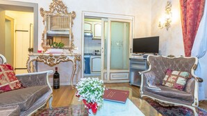 A living room with two sofas, a coffee table, a decorative mirror, a television, and a door leading to a kitchen.
