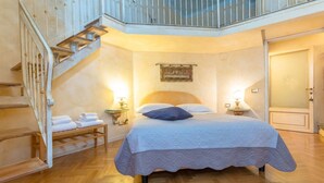 A bedroom with a bed, a wooden bench with towels, a staircase, and a door.