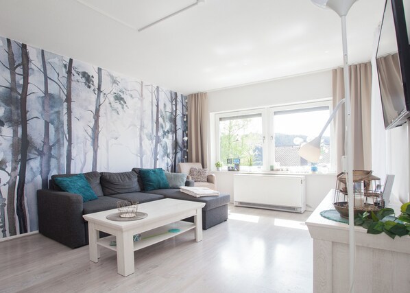 A modern living room with a grey sofa, a white coffee table, and a large window with curtains.