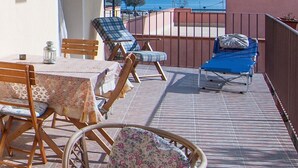 Una terraza con mesa y sillas, vista al mar y barandilla.