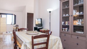 Un comedor con una mesa lista para cuatro, un televisor y un aparador con puertas de vidrio.