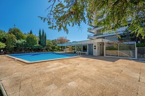 A swimming pool with a covered area, surrounded by trees and a building with balconies.