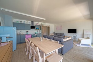 A modern kitchen with a dining area, a gray sofa, and a TV in a living room.