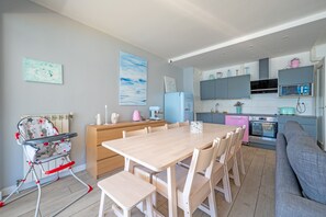 A modern kitchen with a dining area, a high chair, and a sofa.