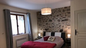 Een slaapkamer met een bed, een stenen muur, een raam met gordijnen, een deur en een hanglamp.
