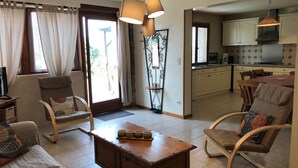 Een woonkamer met een bank, stoelen, een salontafel en een keuken op de achtergrond.
