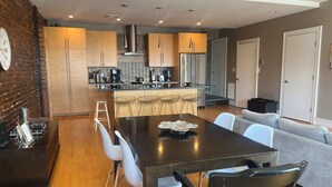 A modern kitchen with wooden cabinets, a central island, and a dining area with a table and chairs. - Boston Harbor views. Modern north end condo.FREE PARKING! (Boston)