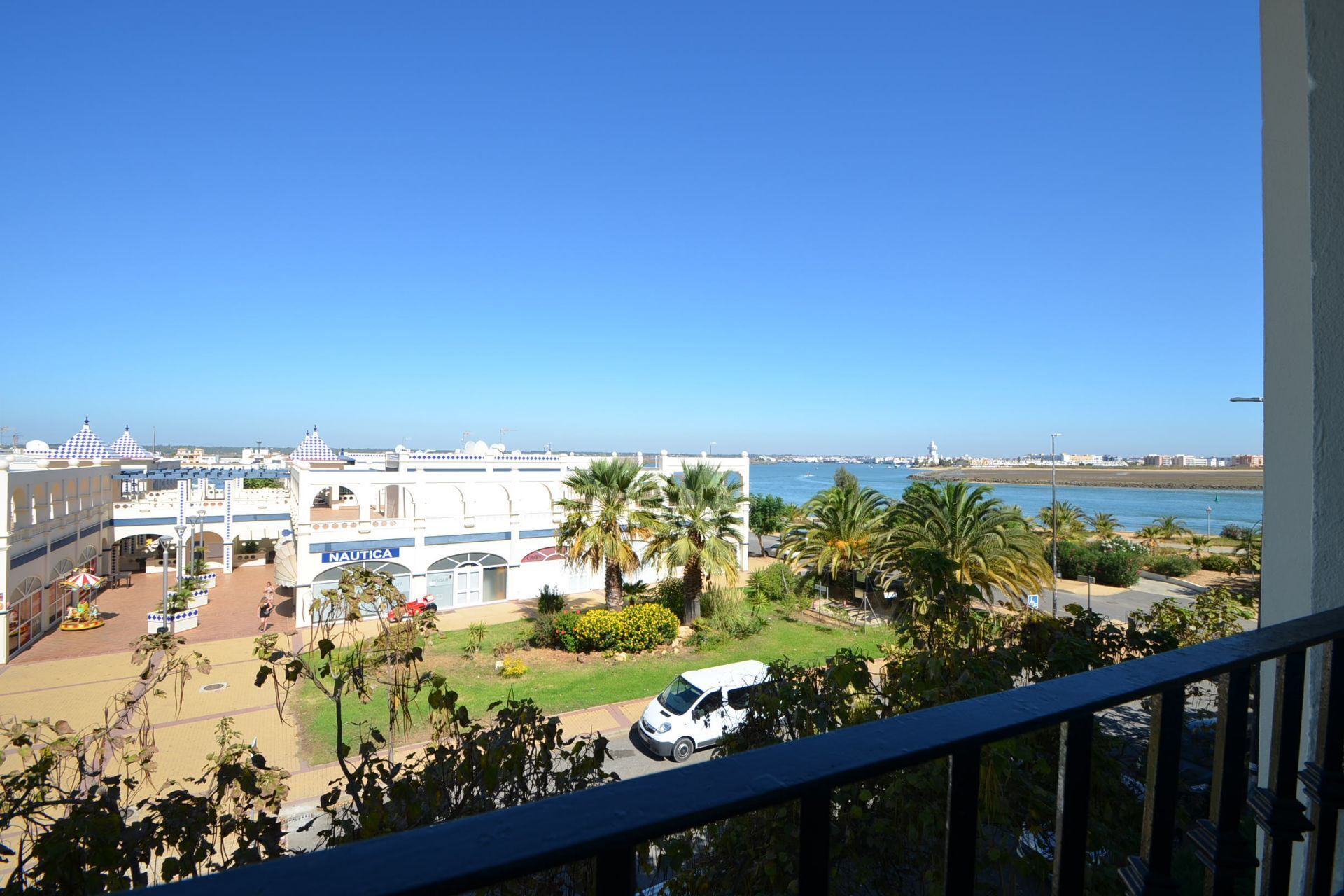 Une vue sur la côte, avec un bâtiment blanc portant l’inscription « NAUTICA », des palmiers et un ciel bleu dégagé.