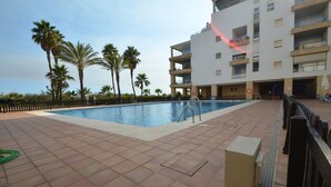 A swimming pool with a modern building in the background, surrounded by palm trees. - Espigón Central 11 - One Bedroom Apartment, Sleeps 3 (Punta del moral)