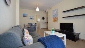 A living room with a grey sofa, a TV, and a small table with a plant. There are two chairs and a dining table in the background. - Espigón Central 11 - One Bedroom Apartment, Sleeps 3 (Punta del moral)
